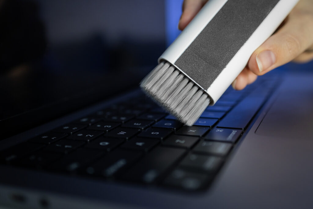 Primer plano de la limpieza del teclado del portátil con cepillo para limpiar el portátil